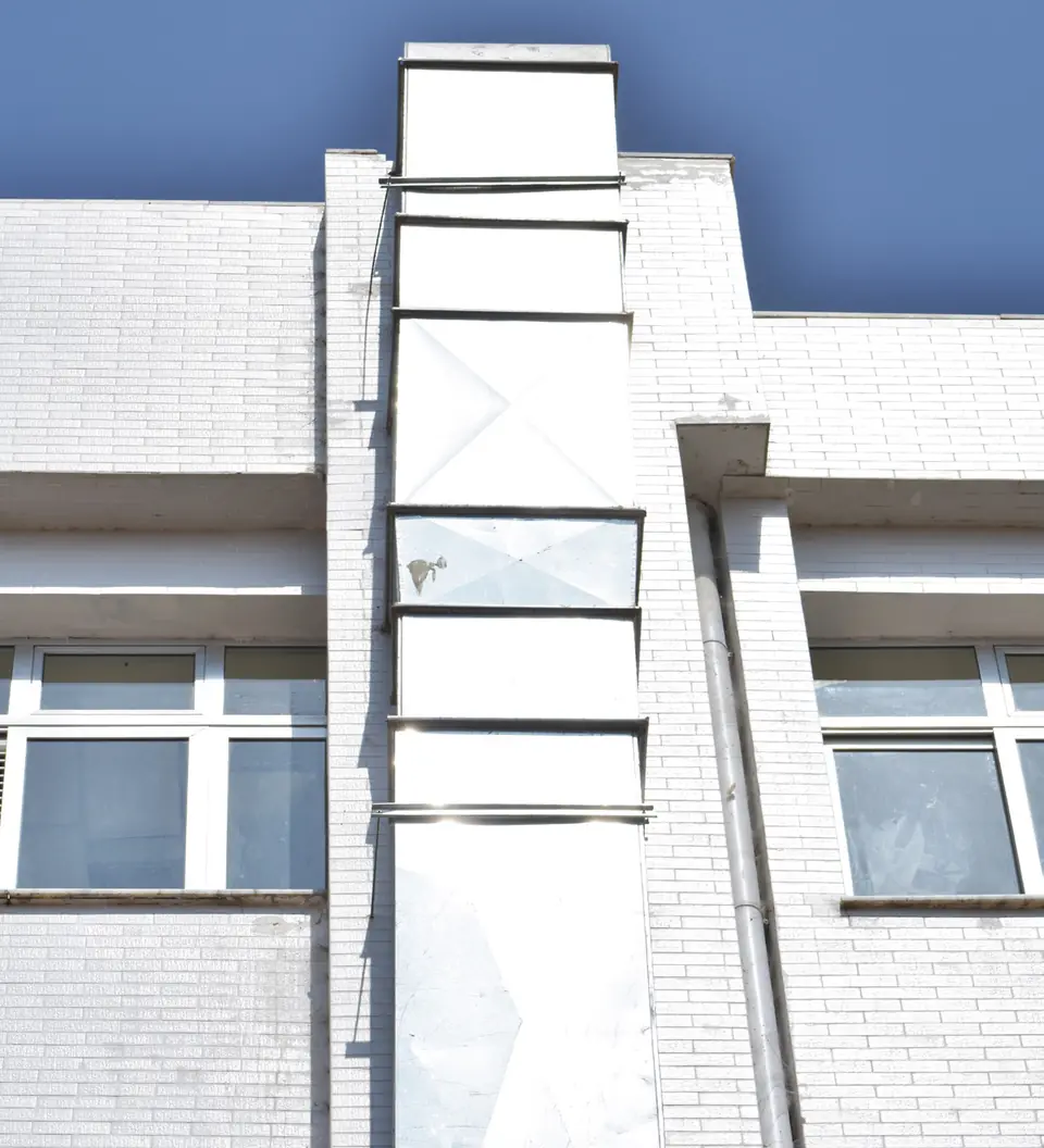 Galvanized duct riser running up the white building facade