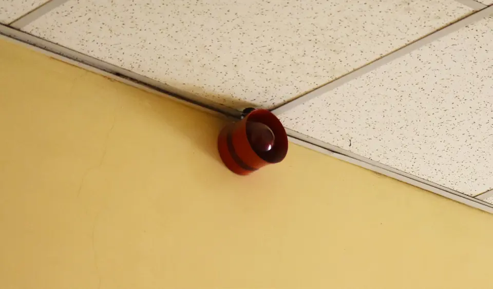 Red fire alarm sounder on a yellow wall